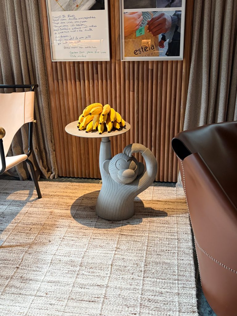 Escultura de macaco no Living Origens, projeto do Atelier Navarro Arquitetura para a CASACOR São Paulo 2026, com bandeja de bananas em ambiente interno.