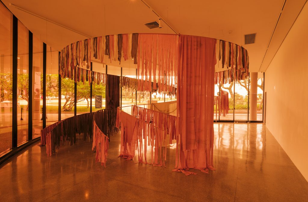 Obra Um dia vou voltar, de Jota Mombaça, com longas faixas de tecido suspensas em uma estrutura circular no Panorama da Arte Brasileira.